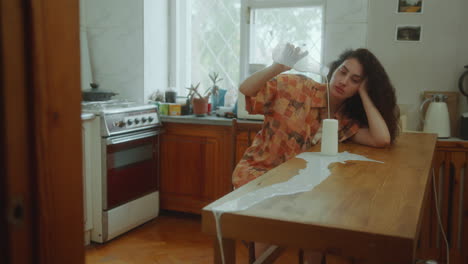 joven deprimida derramando leche en la mesa de la cocina