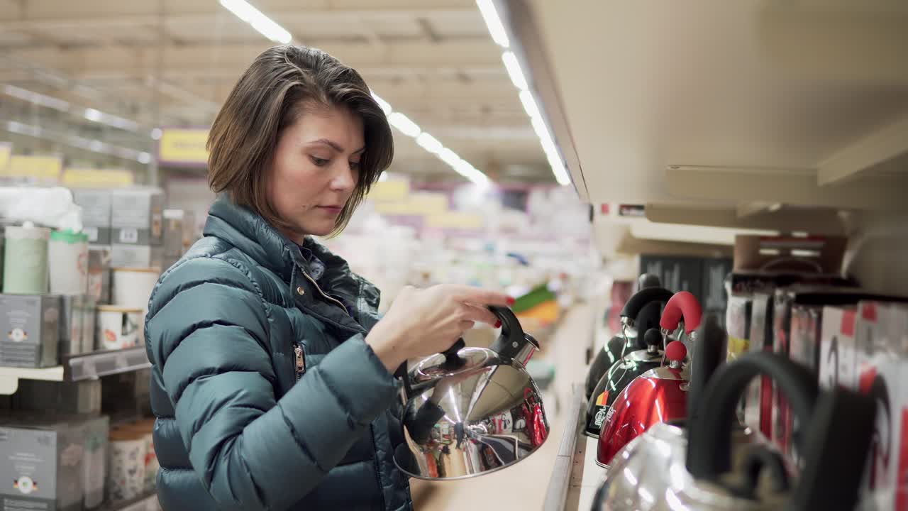 hermosa mujer morena en abrigo elige una tetera en la tienda de electrodomésticos