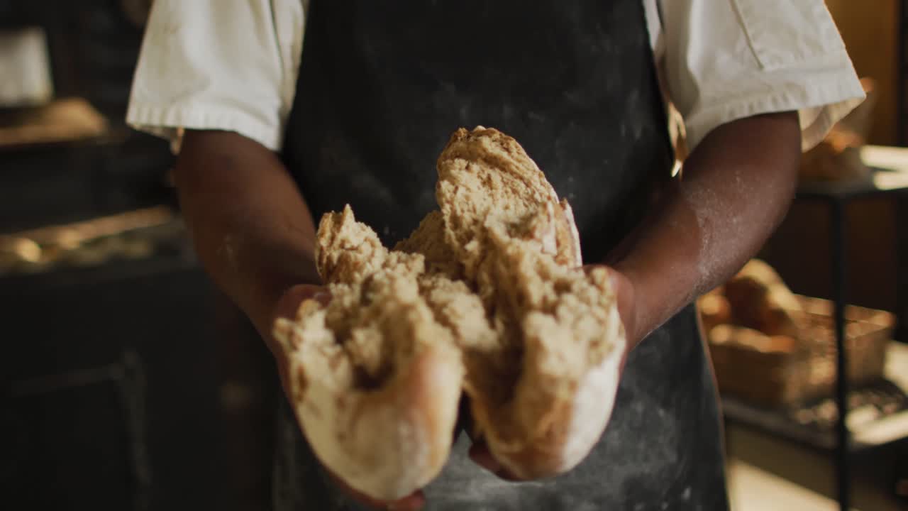 Animation of hands of african american male baker opening freshly baked bread
