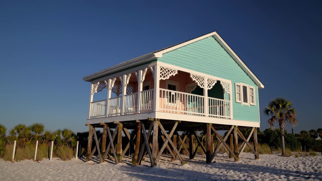 Turquoise stilt house with white porch in Pass a Grille Beach, Florida, showcases a unique architectural style against a backdrop of clear blue sky, evoking a tranquil coastal lifestyle