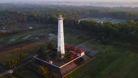 Drone-Orbit-shot-of-white-lighthouse-surrounded-by-flooded-plantation-fields-in-Central-java,-Indonesia