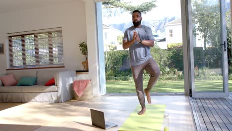 focused african american man practicing yoga using laptop at sunny home, slow motion