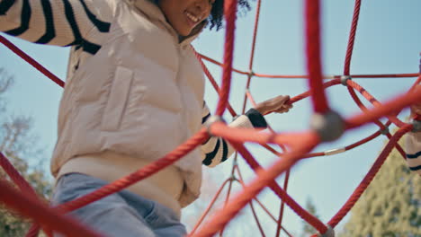 playful mother climbing daughter on rope pyramid at modern playground close up.