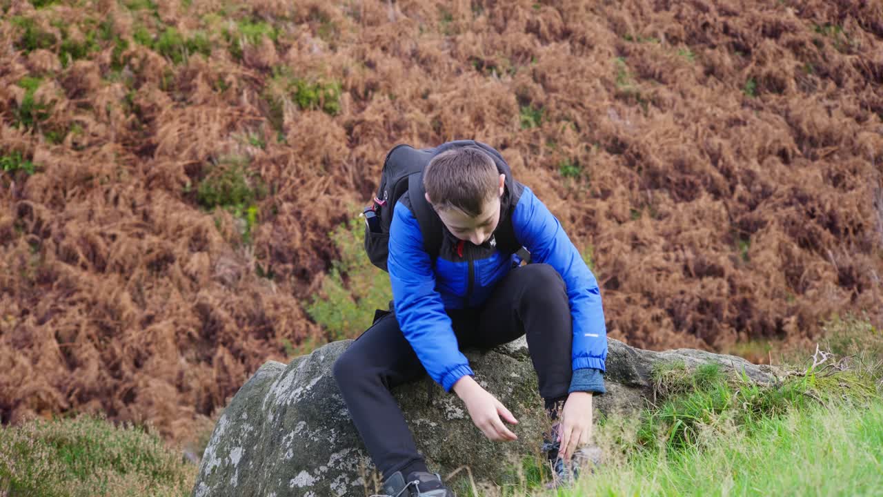 어린 소년이 앉아서 휴식을 취하고, 그의  ⁇ 기 부츠를  ⁇ 고, 가을 야외 풍경 장면에서