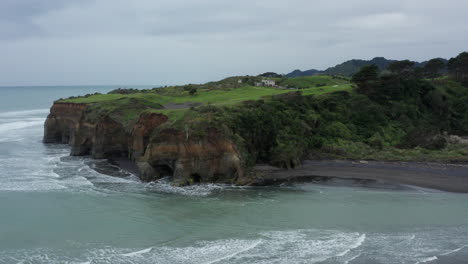 Lush-Cliff-With-Sea-Waves-Splashing-On-The-Shore-At-The-West-Coast-Of-New-Zealand-On-A-Cloudy-Day---ascending-drone-shot