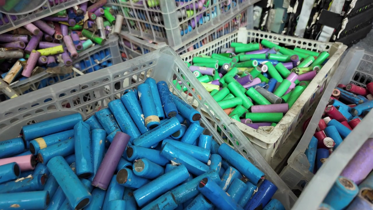 Multiple plastic crates filled with sorted, used 18650 lithium-ion battery cells ready for recycling and processing. Electronic waste (e-waste), sustainable energy management, and battery reuse