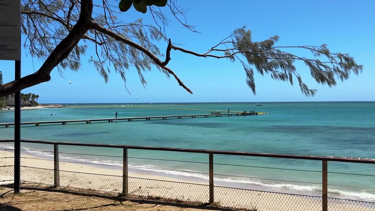 white sandy beach with a jetty extending into the ocean on a bright sunny day blue skies in Noumea, New Caledonia