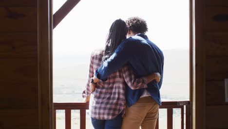 happy african american couple looking through window and embracing in log cabin, slow motion