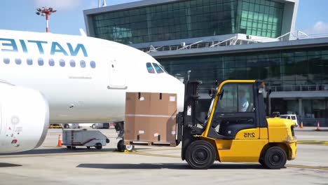 a forklift transporting cardboard boxes alongside an airplane at an airport, showcasing the efficiency of ground logistics operations in air travel