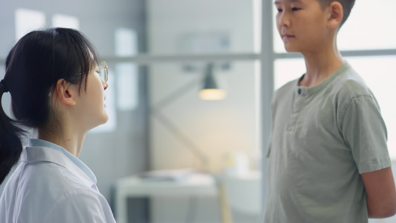 Female Doctor Examining Neck of Asian Boy