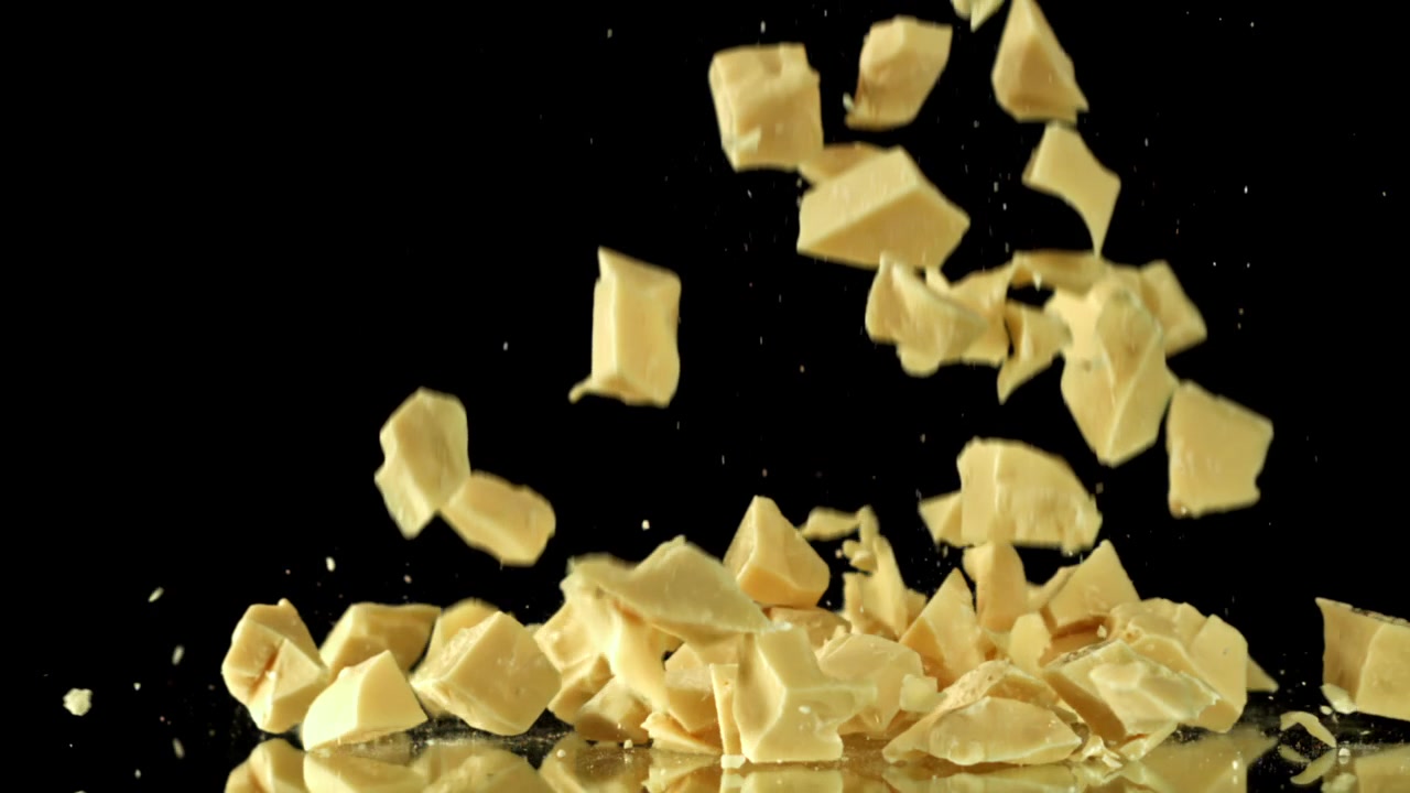 Movimento rallentato di pezzi di cioccolato bianco che cadono su una superficie riflettente