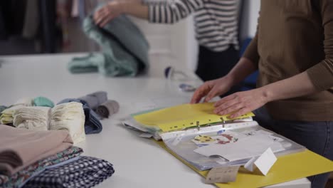 Two-unrecognizable-seamstresses-working-with-sketches-and-fabrics-in-the-studio