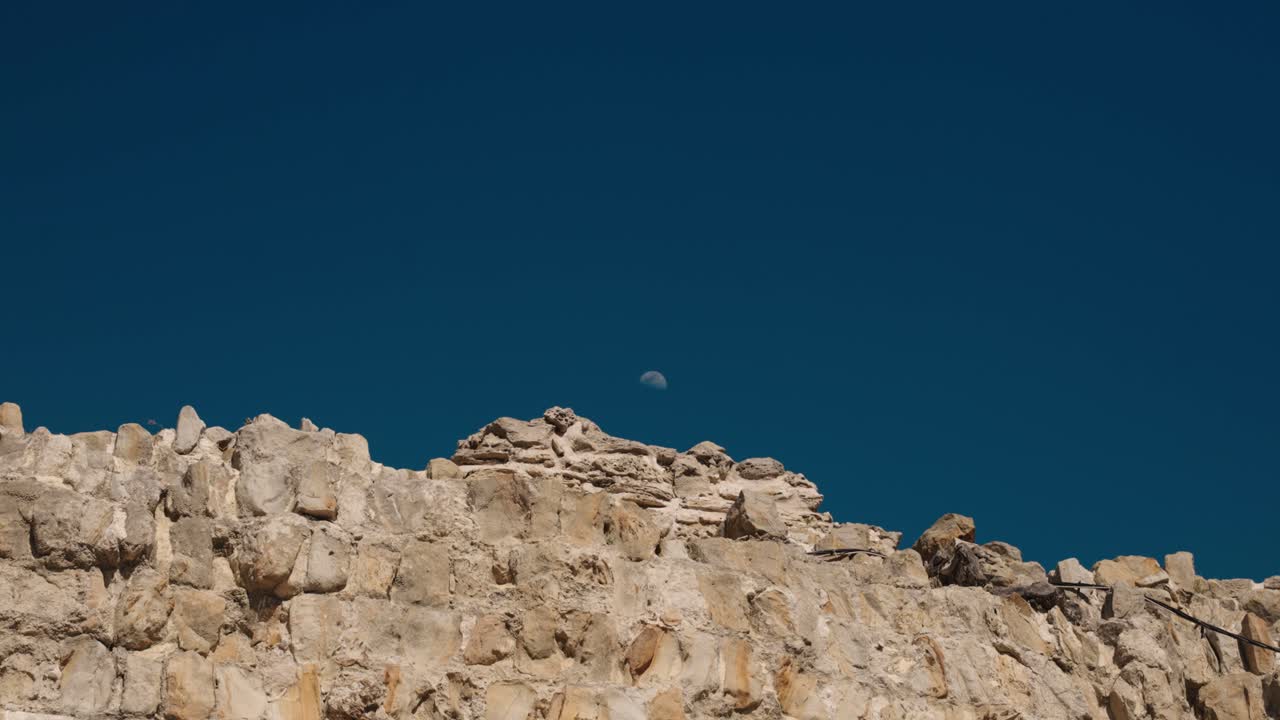 Moon rising above ancient stone fortress wall in Tangier, Morocco under dark sky
