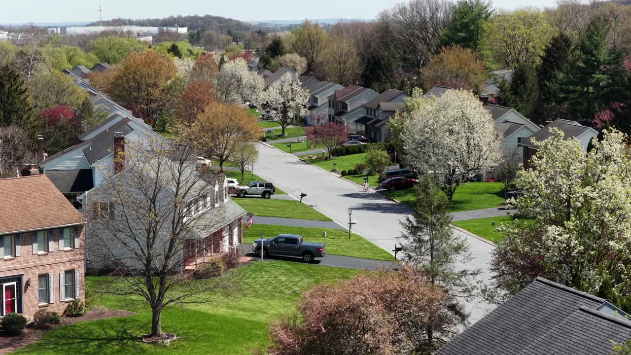 Aerial flyover of peaceful Pennsylvania neighborhood in spring, with detached homes, quiet residential streets, blooming trees, green lawns and bright sunshine in suburban USA. Wide shot