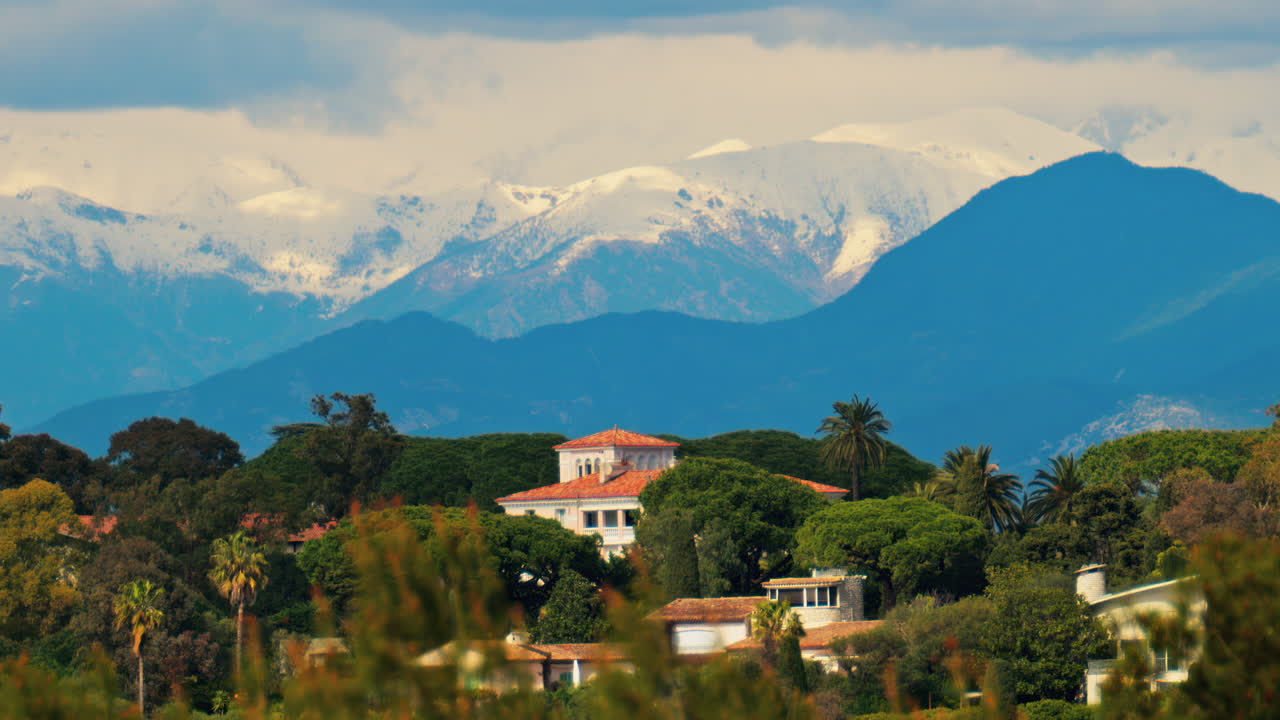 Distant view of orange villas surrounded by green trees with the mountains on the background on a cloudy day