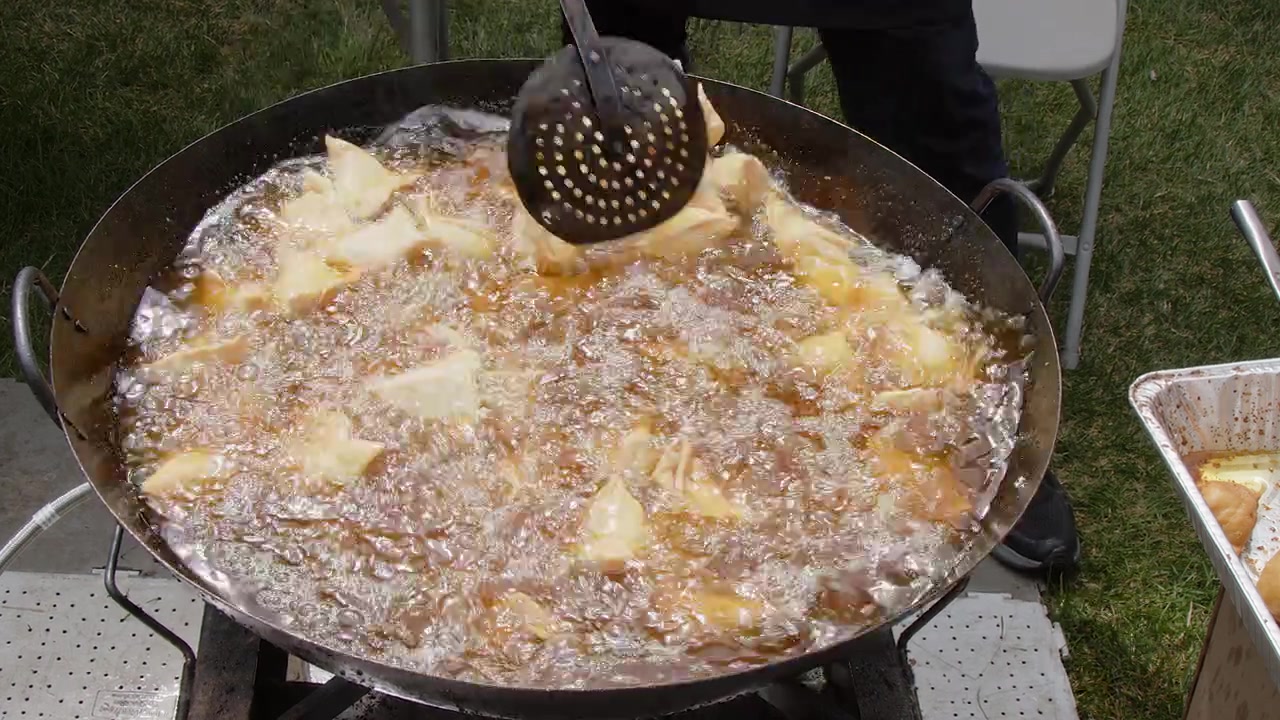 Samosa di verdure fritti in olio bollente in un calderone all'aperto a un festival indiano.