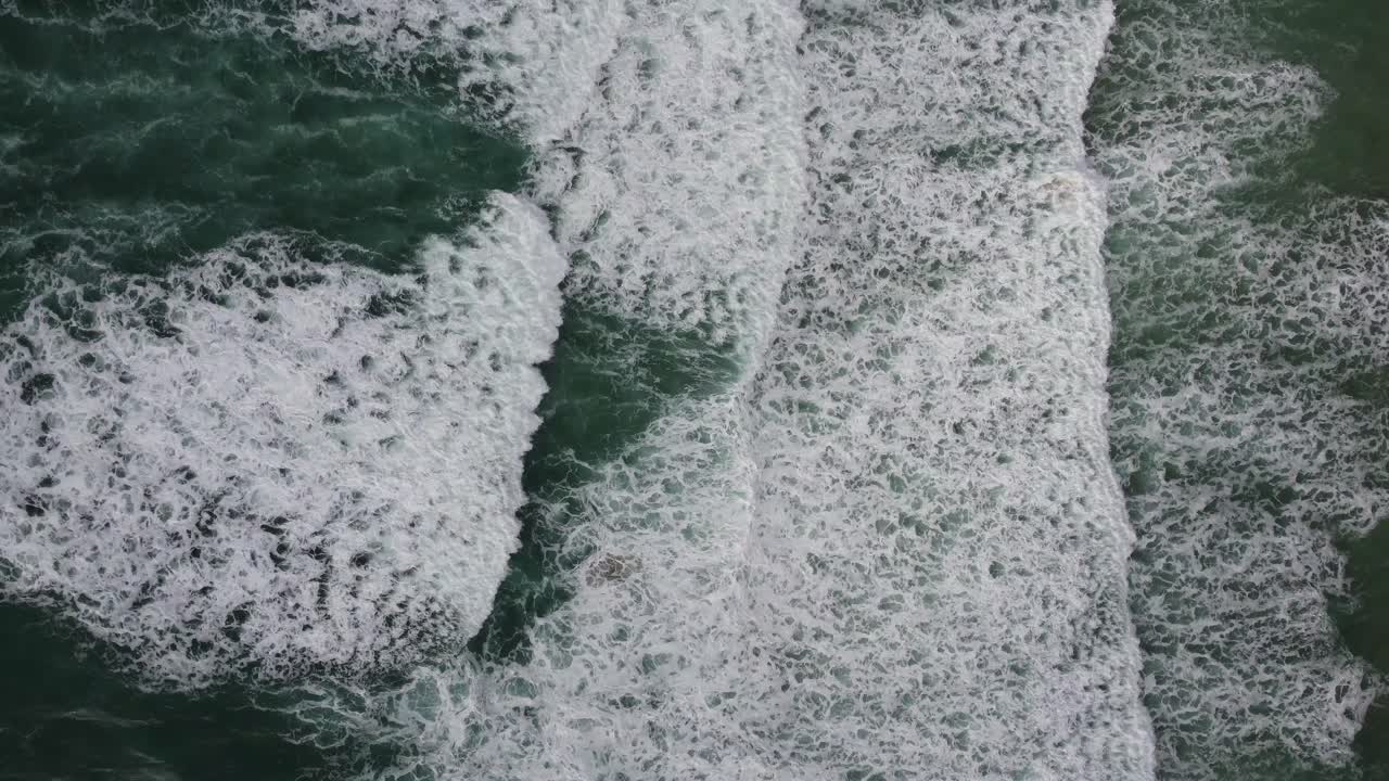A top down cinematic drone shot of green Cornish waves, ideal for surfing, slowly rolling and breaking on the shore
