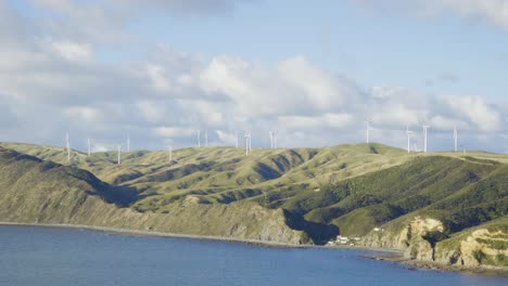 a coastal wind farm spinning high on a hill over the water