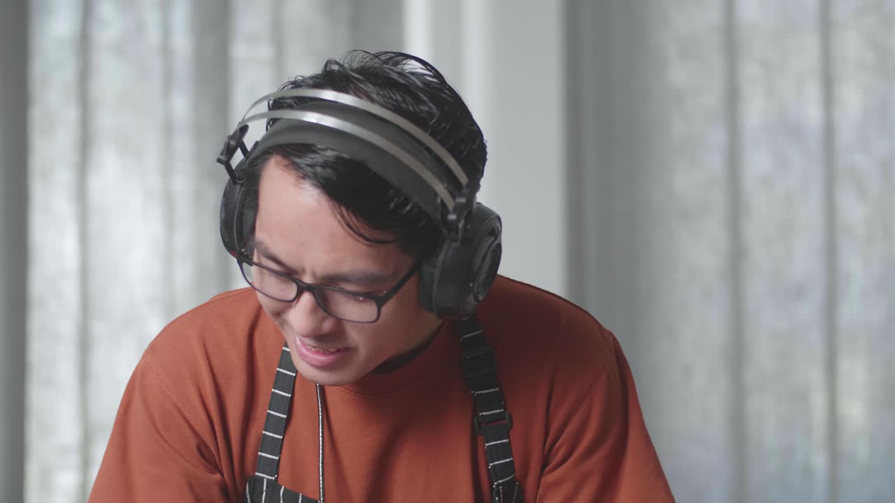 primer plano de una ama de casa asiática con un delantal usando auriculares, escuchando música y bailando mientras aspira el suelo en casa