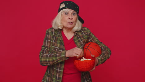 anciana anciana fanática de baloncesto comiendo palomitas de maíz haciendo el gesto del ganador, celebrando la victoria