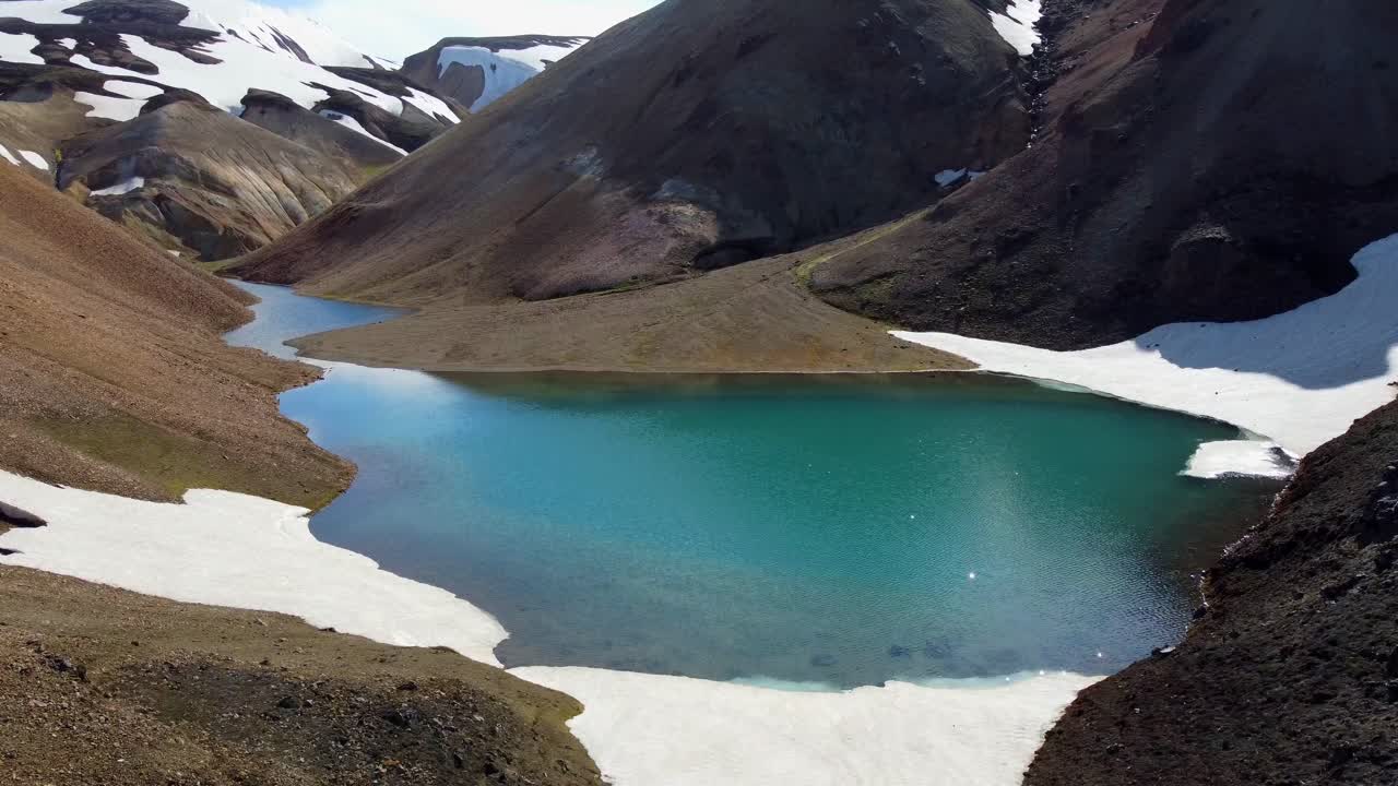 reflejos del sol en un lago de montaña azul entre rocas de magma negro, nieve y piedra rojiza