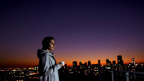 woman enjoying coffee on rooftop at sunset over city