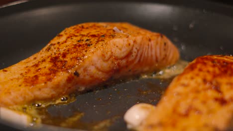 fresh wild caught salmon fish fillets cooking in frying pan skin side down seasoned with cajun spice and salt and pepper with butter and garlic 4k