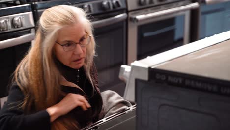 Closeup-of-pretty-mature-blonde-woman-shopping-for-a-stove-at-a-kitchen-appliance-store-showroom