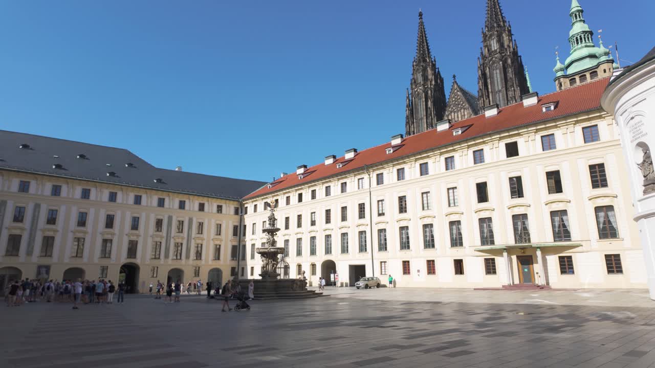 Tourists gather in the Second Courtyard of Prague Castle under a clear blue sky on a sunny day