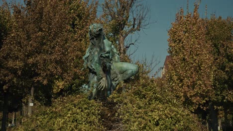 estatua de bronce rodeada de frondoso follaje en el volksgarten, viena, austria