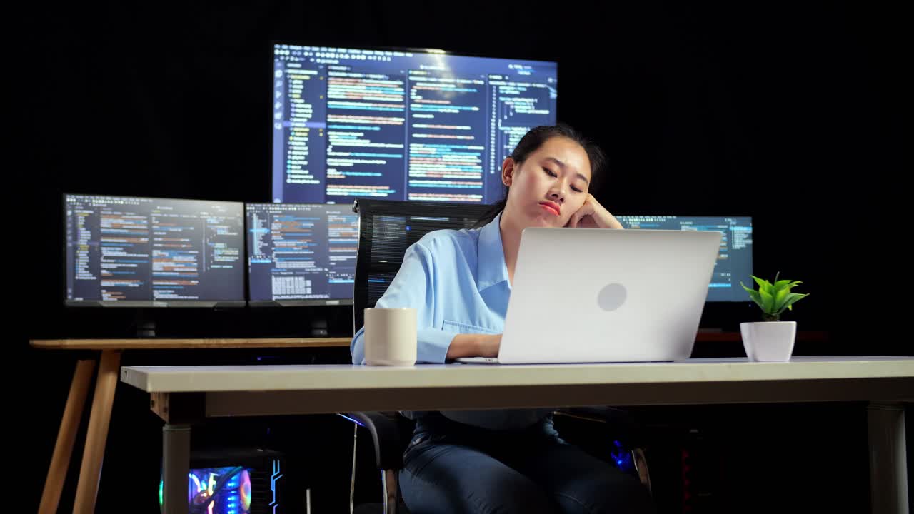Asian Female Programmer Being Bored Writing Code By A Laptop Using Multiple Monitors Showing Database On Terminal Window Desktops In The Office