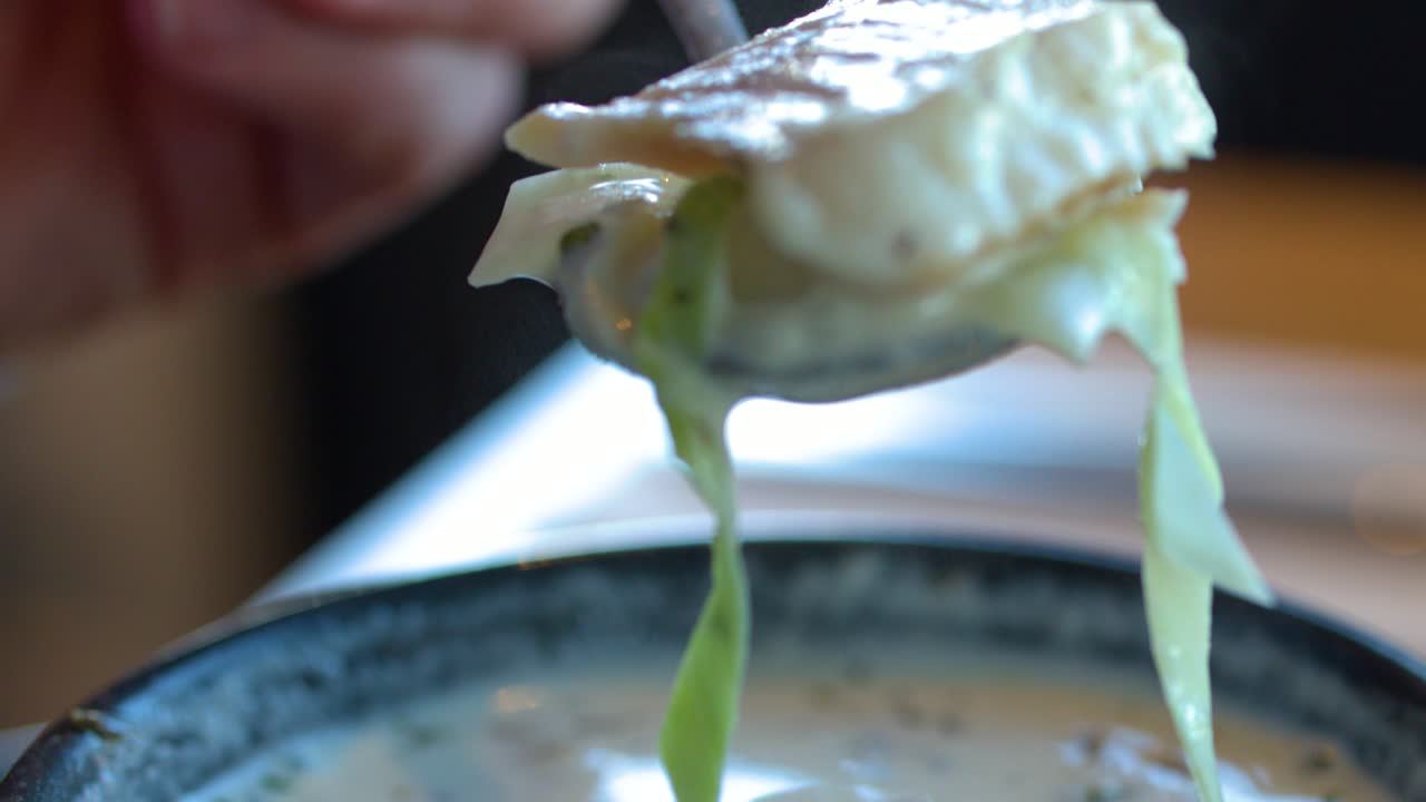 Hand lifts spoonful of creamy fish soup with leeks in natural light, shallow focus