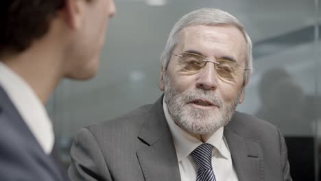 mature businessman in eyeglasses talking to younger colleague