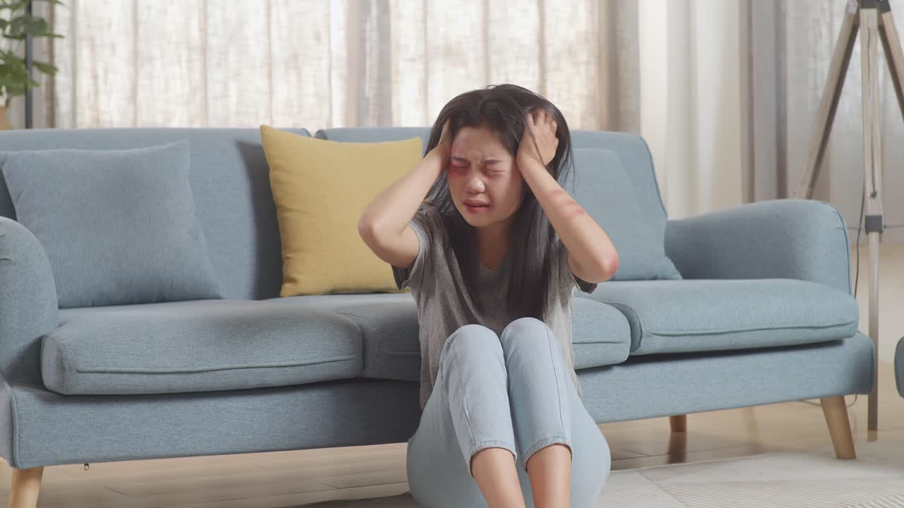 몸에 이 있는 폭력의 희생자인 젊은 아시아 여성은 집에서 바닥에 앉아있는 동안 신경약과 비명을 지르고 있습니다.