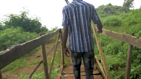 a slow motion tracking shot of a young african man crossing over a wooden foot bridge in tropical east africa