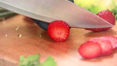 slicing fresh strawberry on a wooden board with a large knife into slices, close up of cook hands with black gloves