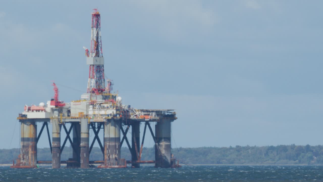 Offshore oil drilling platform in rough sea under overcast sky, viewed from shore, Cromarty, Scotland