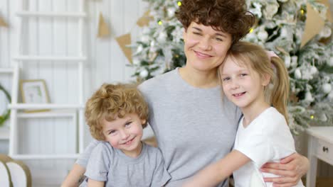 Hermosa-Madre-Abrazando-A-Sus-Hijos-Pequeños-Y-Sonriendo-A-La-Cámara-En-Navidad