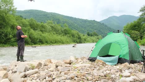 a man controls a drone on vacation near a mountain river a man controls a drone on vacation near a mountain river a tent is spread out on the river bank