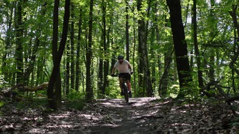 A-static-shot-in-slow-motion-of-an-adult-male-jumping-on-an-electric-bicycle-on-trails-in-the-forest-on-at-sunny-day