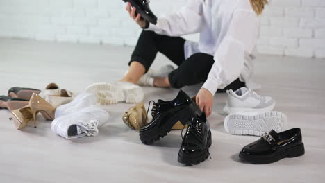 new black, white, beige shoes scattered on the floor. woman in white shirt chooses footwear among the variety.