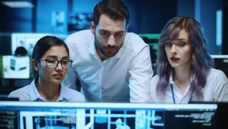 three professionals analyzing data on computer screen in a dimly lit office environment, expressing concentration and collaboration on a project