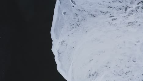 Vista-Superior-Aérea-De-Las-Olas-Espumosas-Del-Océano-Que-Llegan-A-La-Playa-De-Arena-Negra-En-Islandia