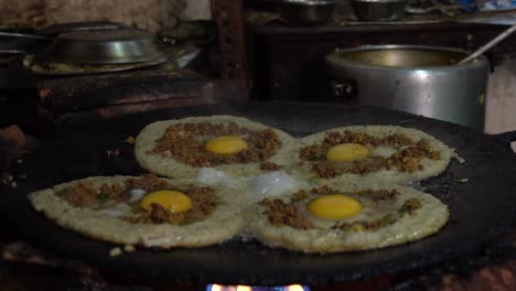 frying newari bara with eggs and meat on a skillet over a fire