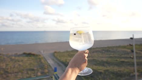 Cóctel-De-Gin-Tonic-En-Una-Terraza-Sostenida-Por-Una-Mujer-Con-Hermosas-Y-Sorprendentes-Vistas-Al-Mar.