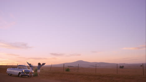 amigas bailando al atardecer en un viaje por carretera con un coche antiguo