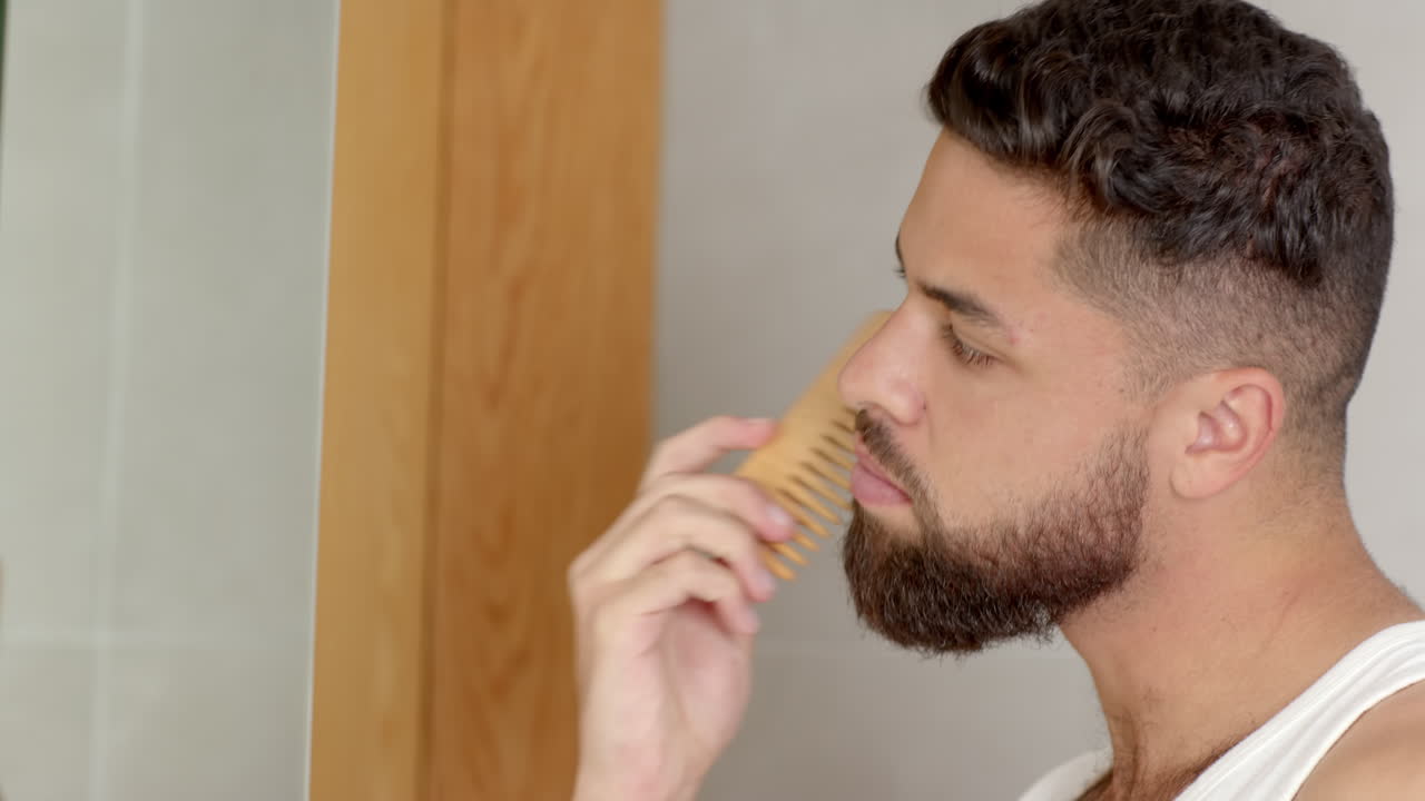 Grooming beard, man using comb in bathroom mirror, focusing on appearance