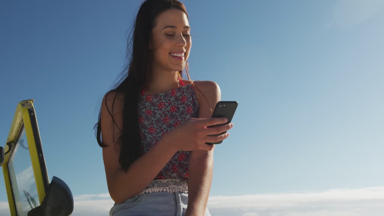 mujer caucásica feliz sentada en un buggy de playa junto al mar hablando en un teléfono inteligente
