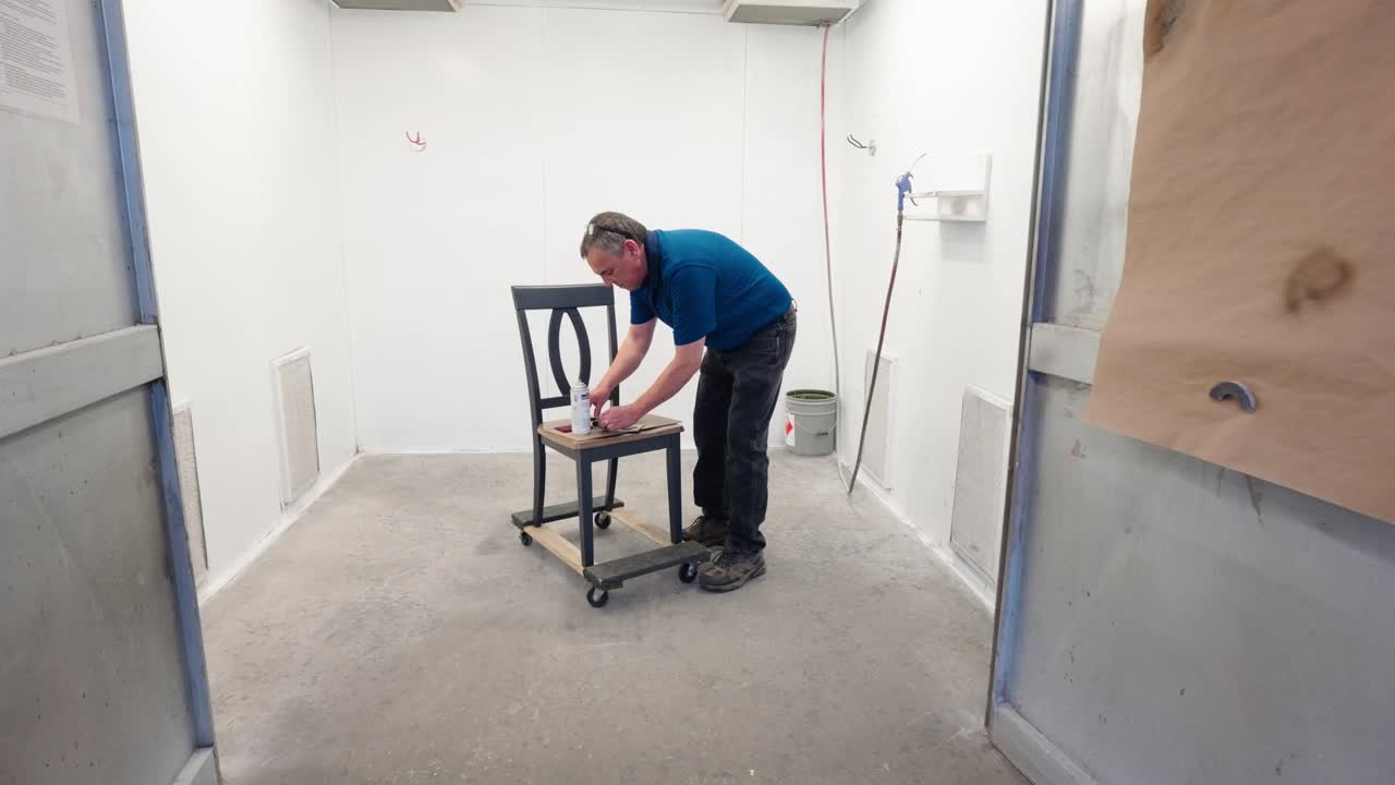 Camera pushes in as worker mixes paint on palette placed on the chair seat