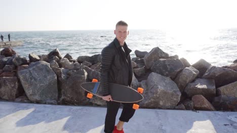 un joven camina con su tabla larga junto al mar